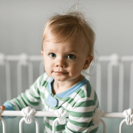Baby in pajamas standing at crib