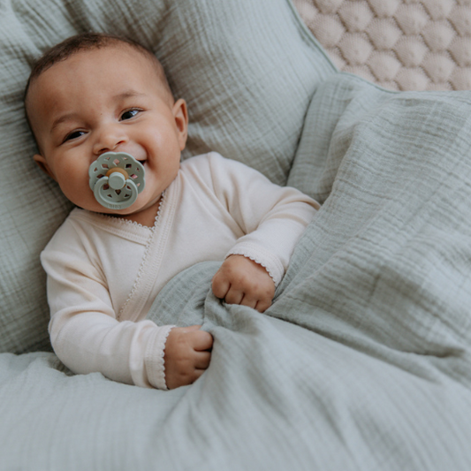a baby laying down smiling with a bibs pacifier