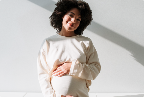 A pregnant woman with curly hair cradling her belly
