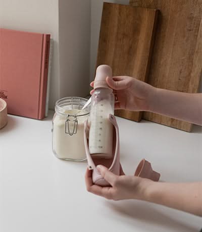 Hands preparing a baby bottle with milk next to a kitchen counter