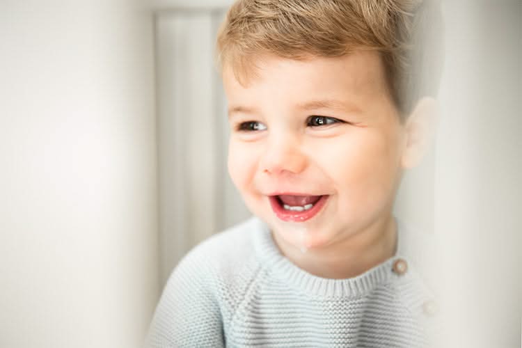 A toddler wearing a beige sweater smiles for the camera