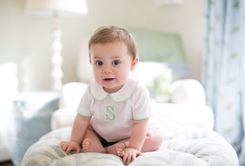 Baby wearing a white shirt with a green-trimmed collar monogrammed with an 's'