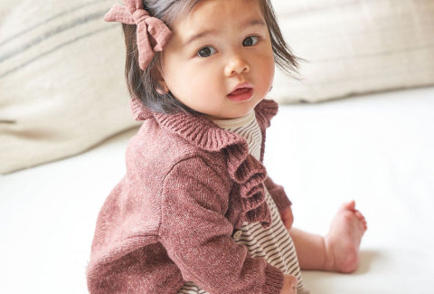 Baby sitting in a pink sweater with a bow hair accessory