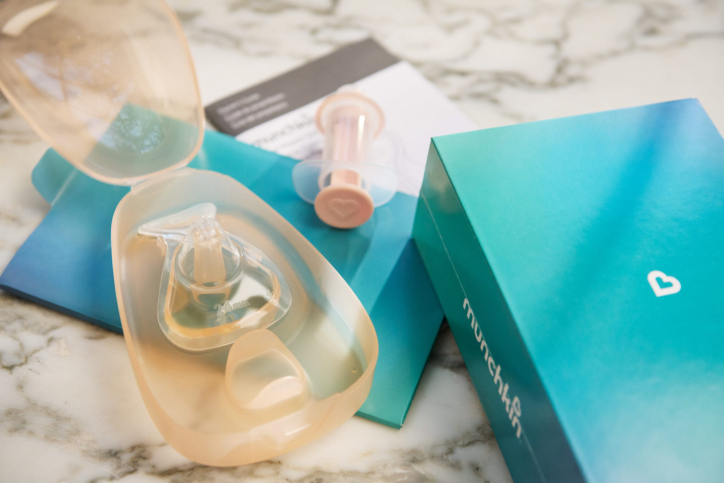 Clear baby bottle with accessories on a marble surface, featuring the Munchkin brand.