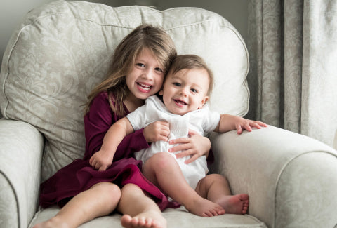 A girl in a burgundy dress and a toddler in a white outfit smiling