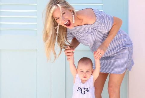 A joyful woman in a striped dress playfully holds up a baby in a matching outfit