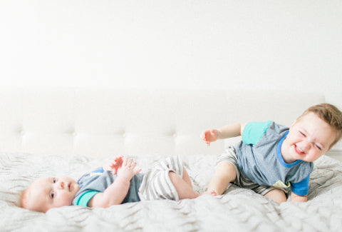 Toddler and baby laughing while lying in bed