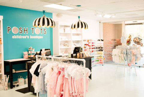 Interior of "posh tots" children's boutique, featuring racks of pastel children's clothing