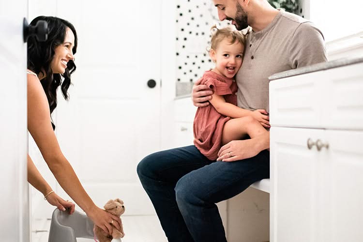 Woman smiling at a toddler held by a man sitting on the tub edge