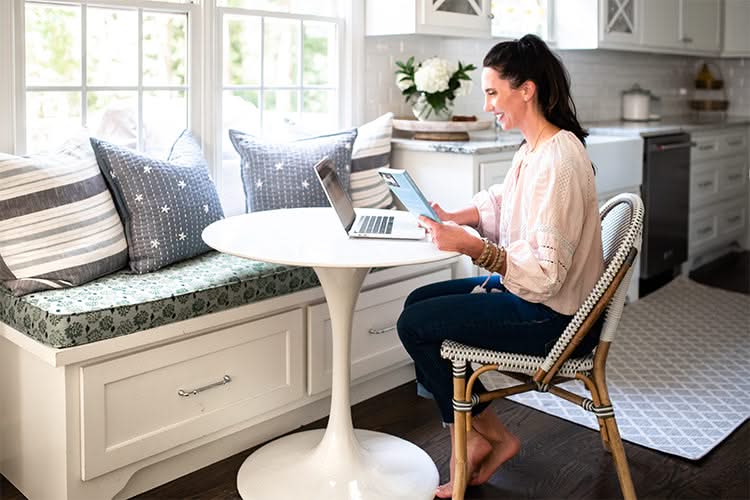 Woman holding a book and looking at a laptop while sitting at a table