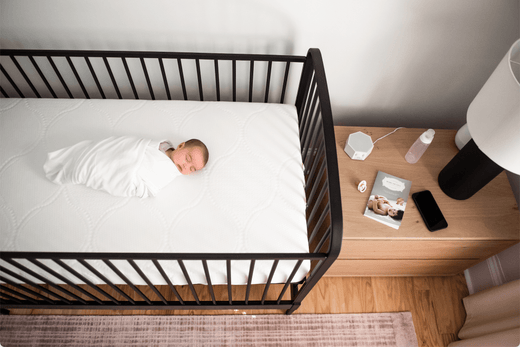 Baby fast asleep in their crib with a Moms on Call book on the night stand. 