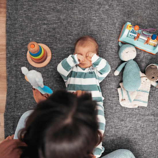 Tired baby rubbing eyes while playing with toys