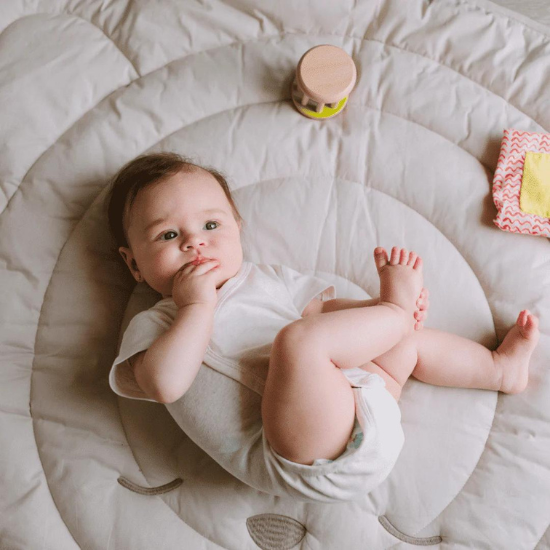 Baby in onesie on play mat with toys