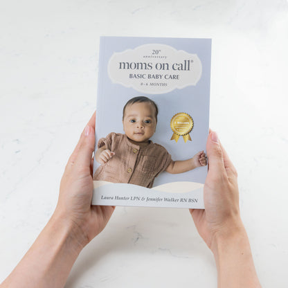 Book titled 'Moms on Call: Basic Baby Care' held by a person against a white background